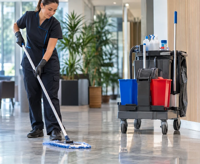 Agente utilisant un balai à plat avec un chariot de lavage dans un hall professionnel.